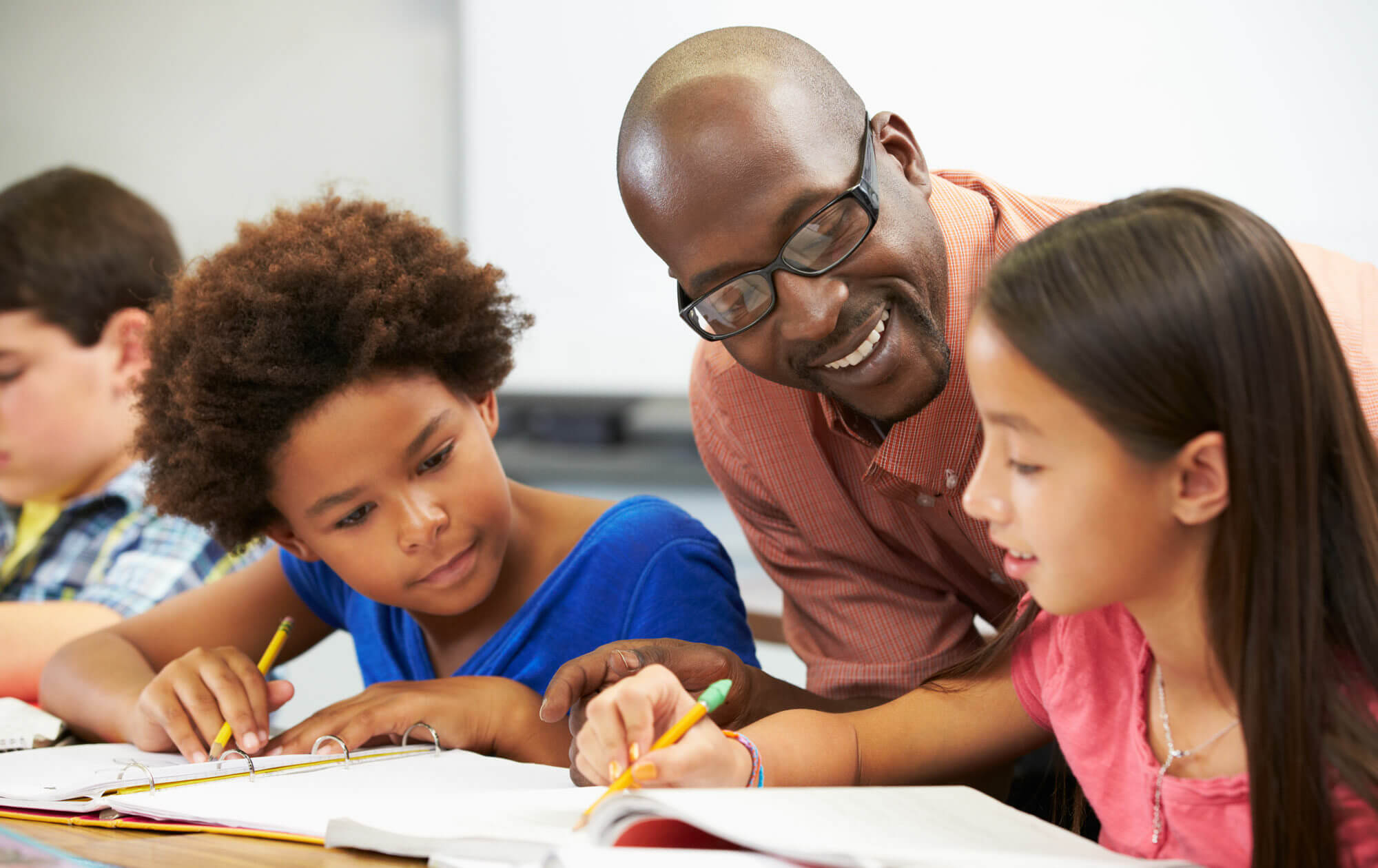 Smiling teacher encourages middle school students as they write in their phonics workbooks