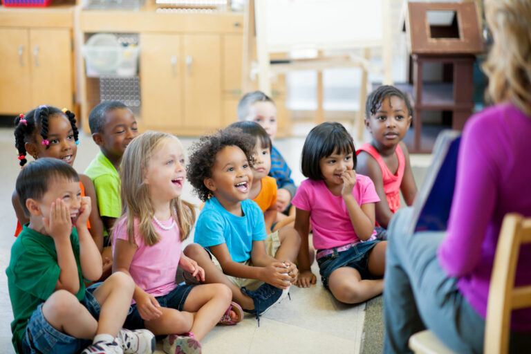 small group of elementary school students sits around teacher reading a book