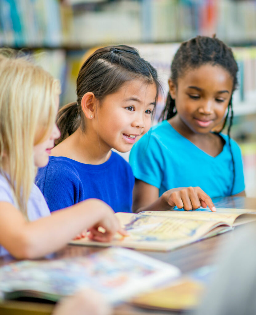 Three elementary school girls point to words they are breaking into parts and reading