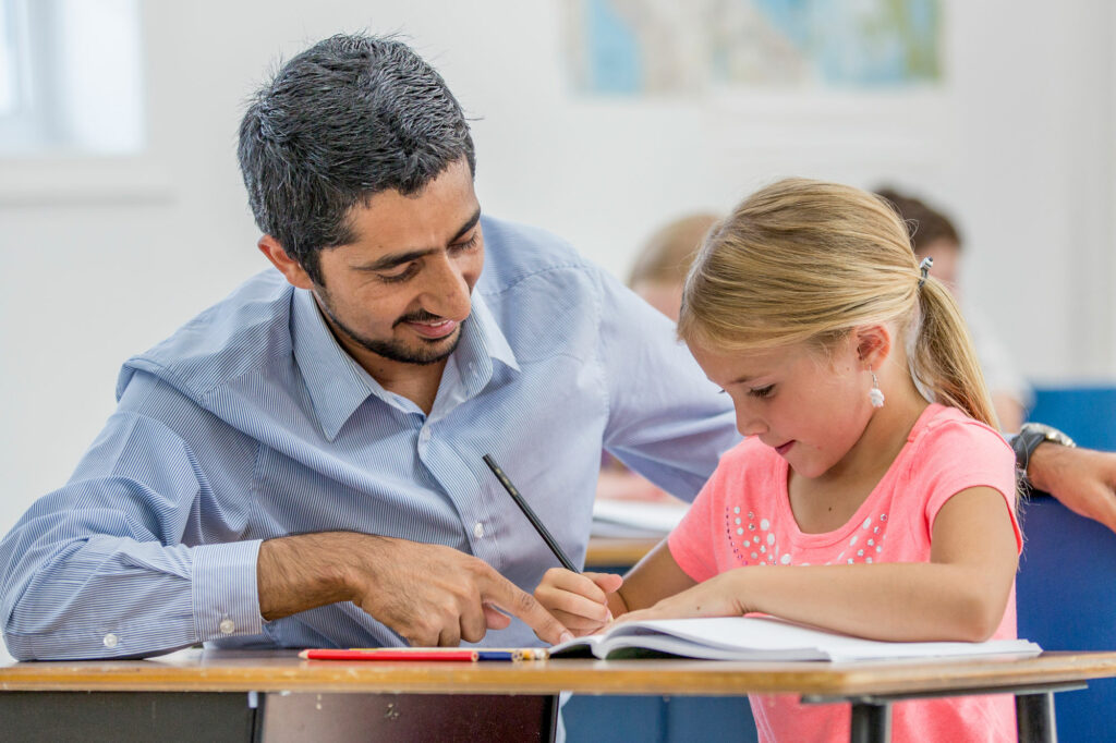 A teacher guides his elementary-school student through written workbook exercises