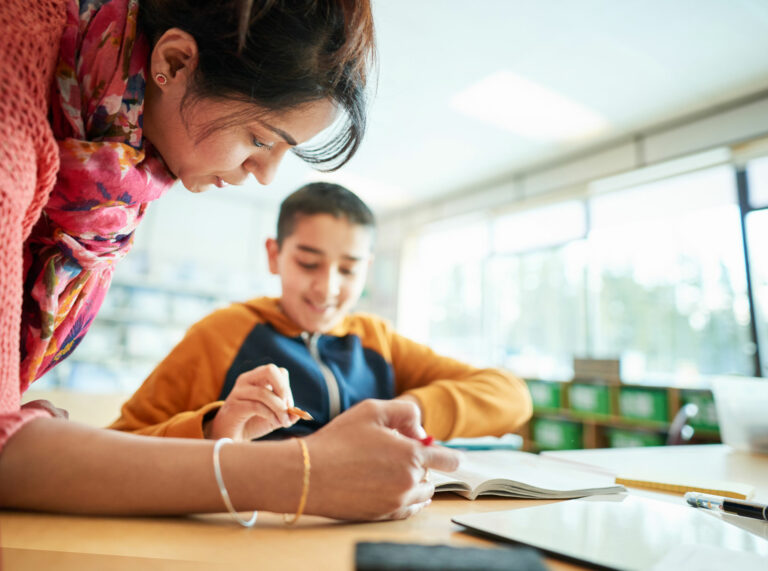 teacher bends down to assist with phonics workbook lesson with student