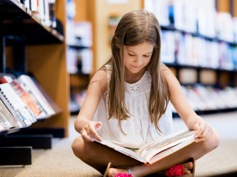 A middle school student sits on the library floor, reading her book