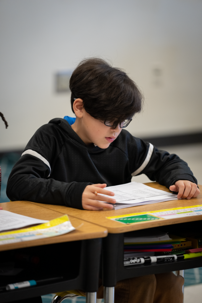 A focused middle school student sounds out multisyllable words on a worksheet