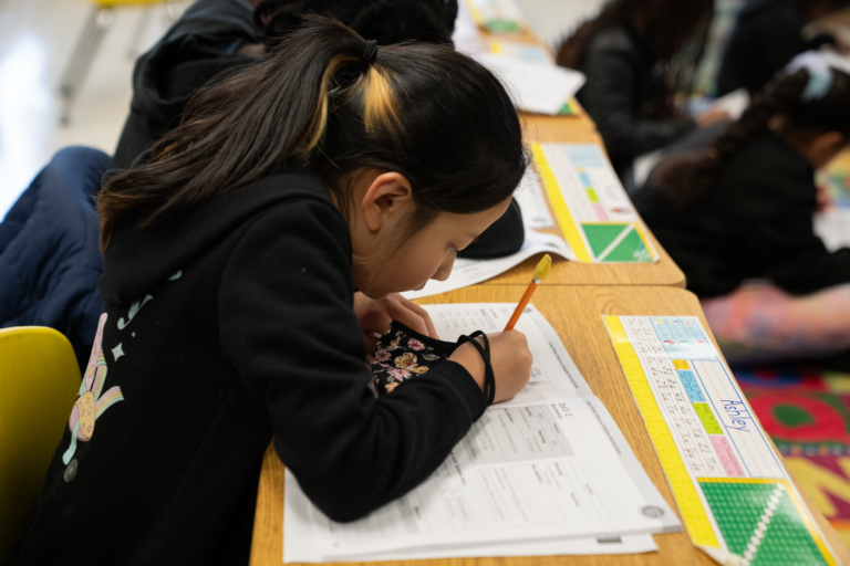 Student sitting at deck writing in a phonics workbook.