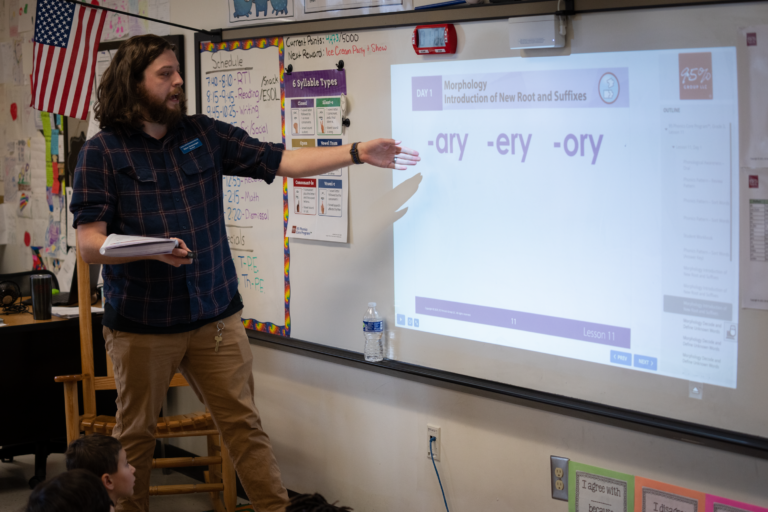 Teacher pointing to white board with Morphology, Introduction of New Root and Suffixes.