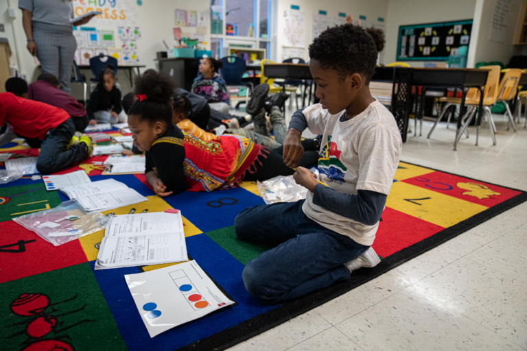 Children on a rug, free to move around as they use their chip kits and spelling mats