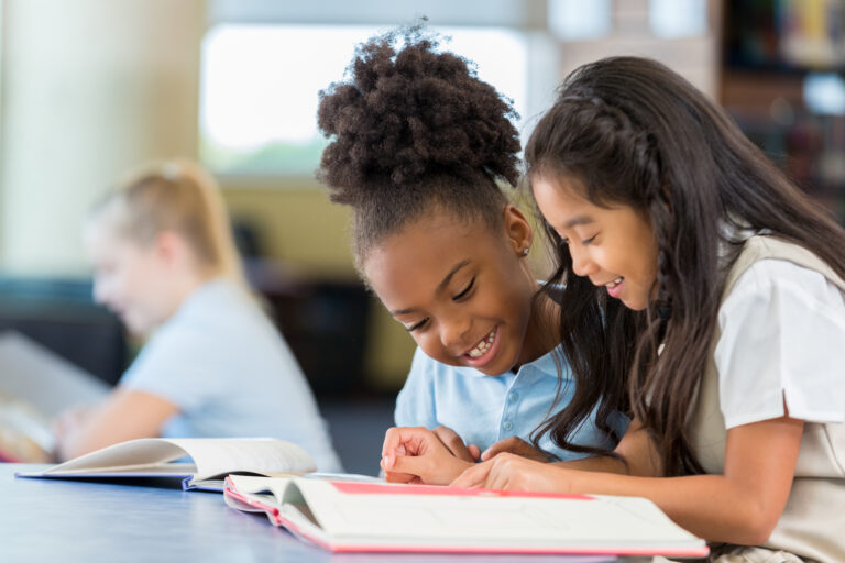 Girls reading a book together at school, pointing out words