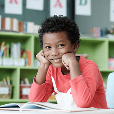 Happy elementary school boy looking up from his reading in a classroom