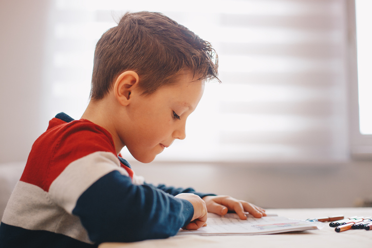 young boy follows along phonics workbook at his desk