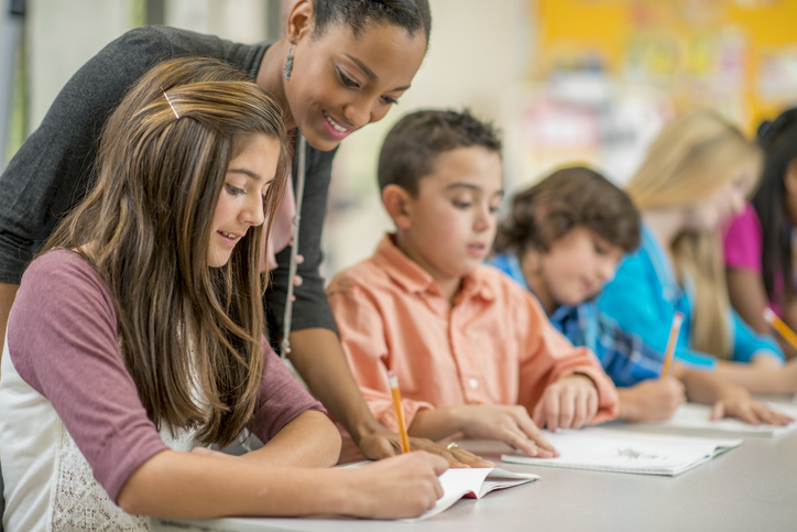 Teacher standing over students while they are engaged in an activity.