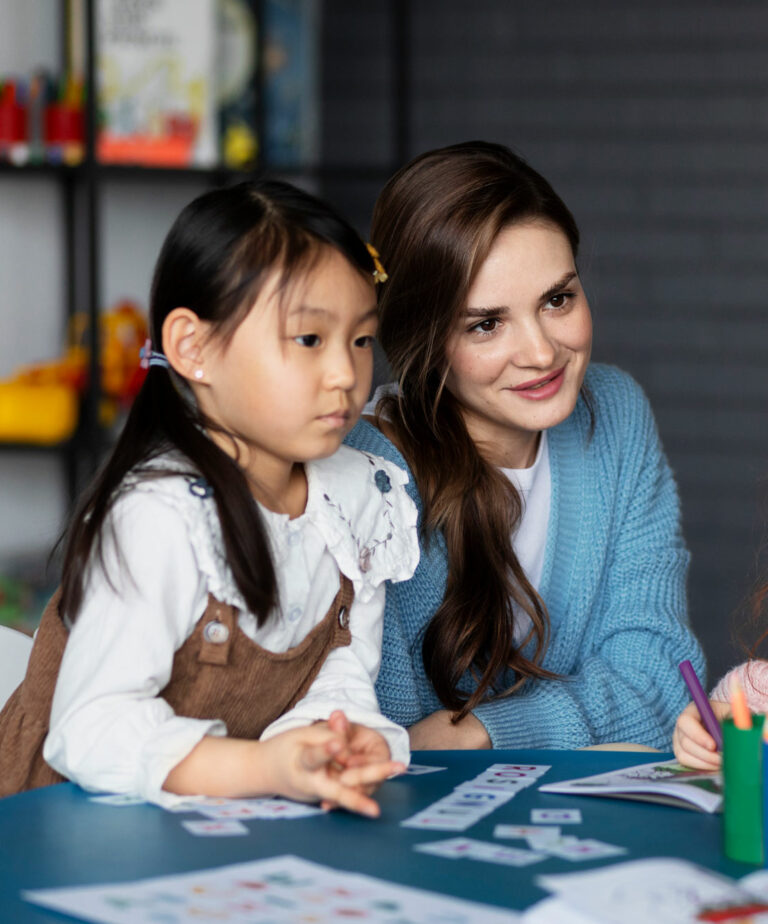 Two girls with phonics spelling mats look toward their reading specialist