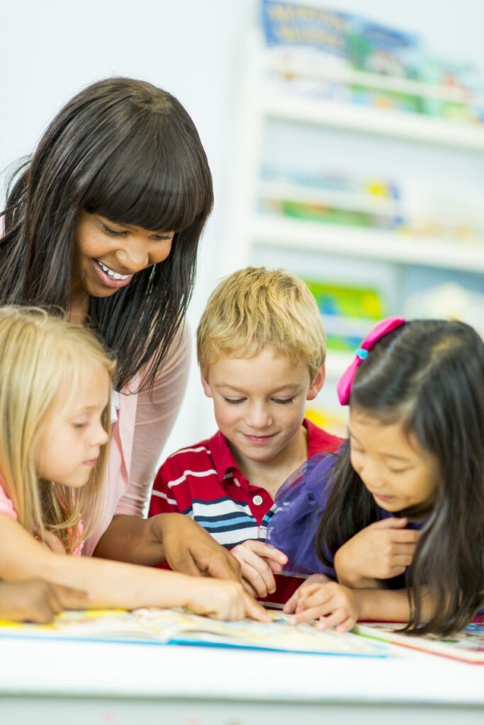 young teacher eagerly helps her elementary students with a reading activity