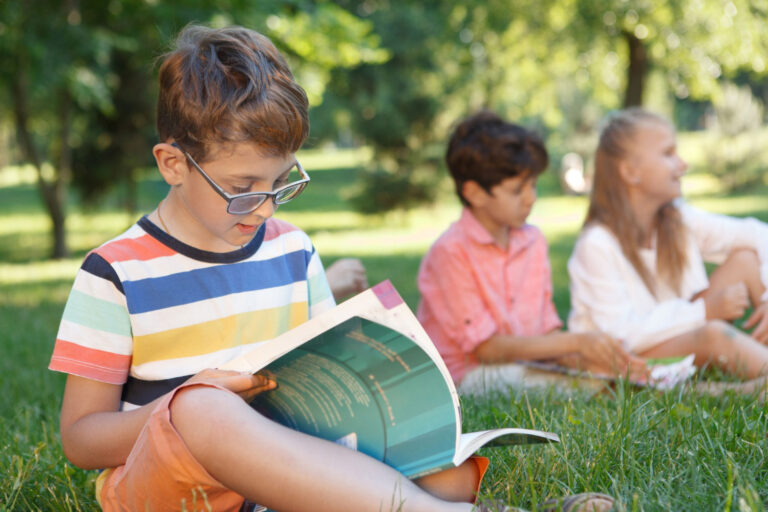 grade school boy reading a book outside with his friends, reducing summer slide in literacy
