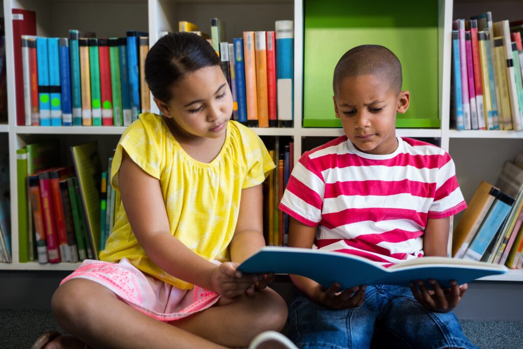 latina and african american elementary school kids reading a book together in a school library