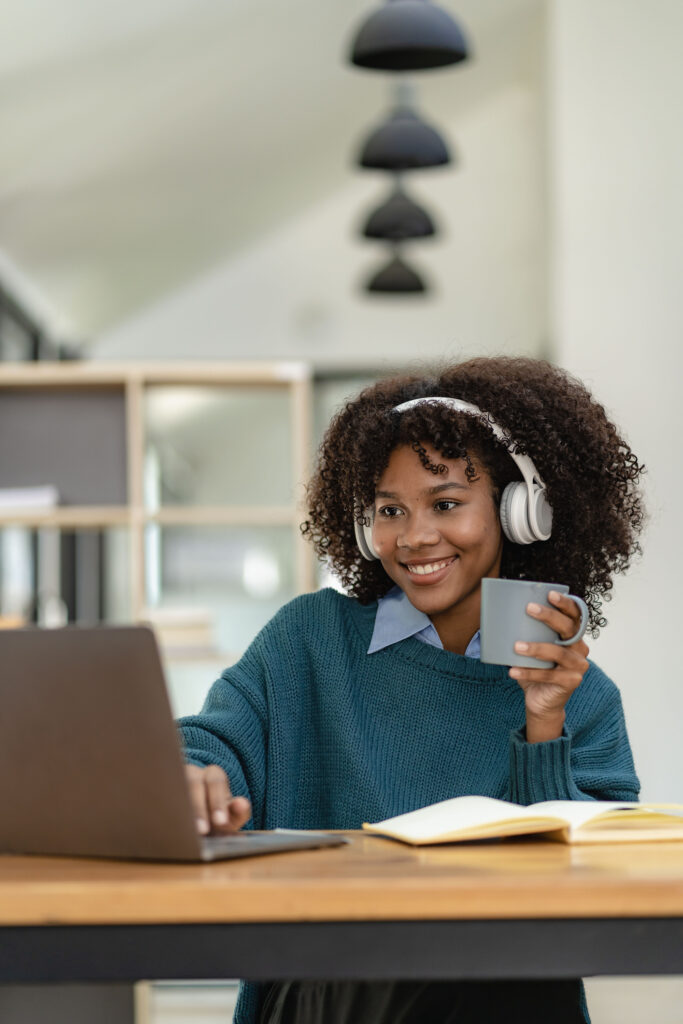 young, african american, female classroom teacher accessing online, phonics workshop on her laptop, holding a cup of coffee