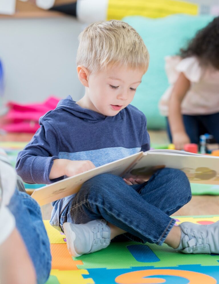 Child reading a book while sitting on a colorful play mat