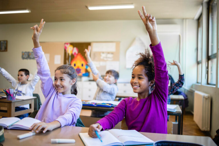 elementary students raising hands in classroom