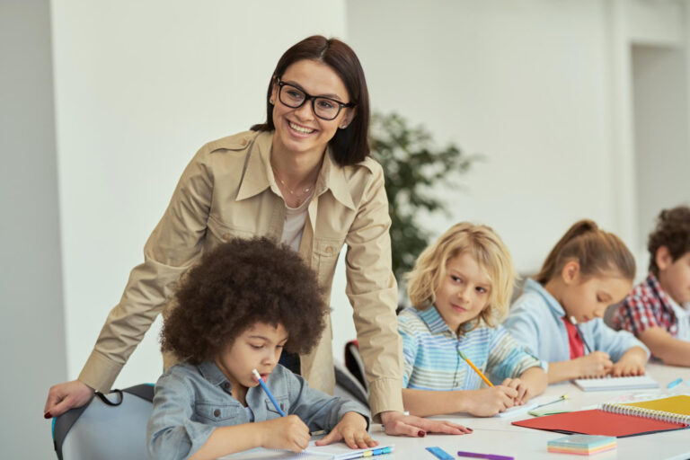 young female teacher in glasses smiling while helping little students kids