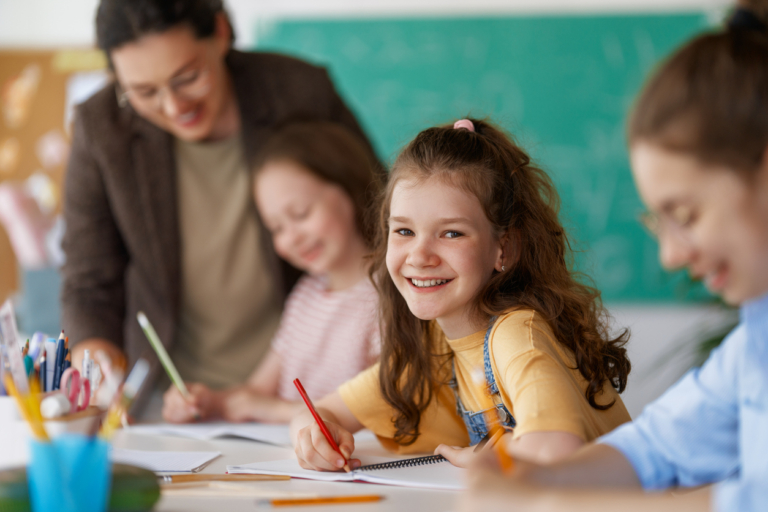 Happy kids and teacher at school. Woman and children are working in the class.