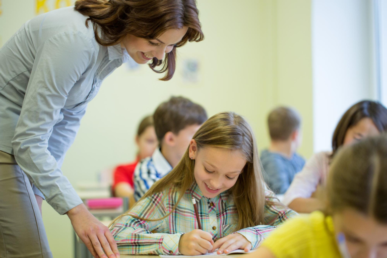 teacher helping school girl in class reading lesson